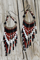 A pair of handmade beaded dangle earrings with black, white, and red beads.
